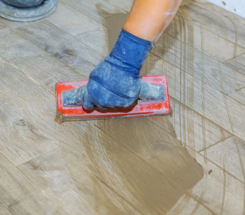 hand-of-flooring-on-gray-color-of-new-grout-tile-on-tile-gray-for-the-final-step-for-flooring.jpg